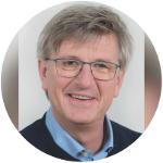Ein Mann mit grauen Haaren und einer Brille, er lächelt