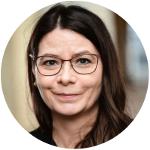 Eine Frau mit dunklen langen Haaren und Brille lächelt in die Kamera