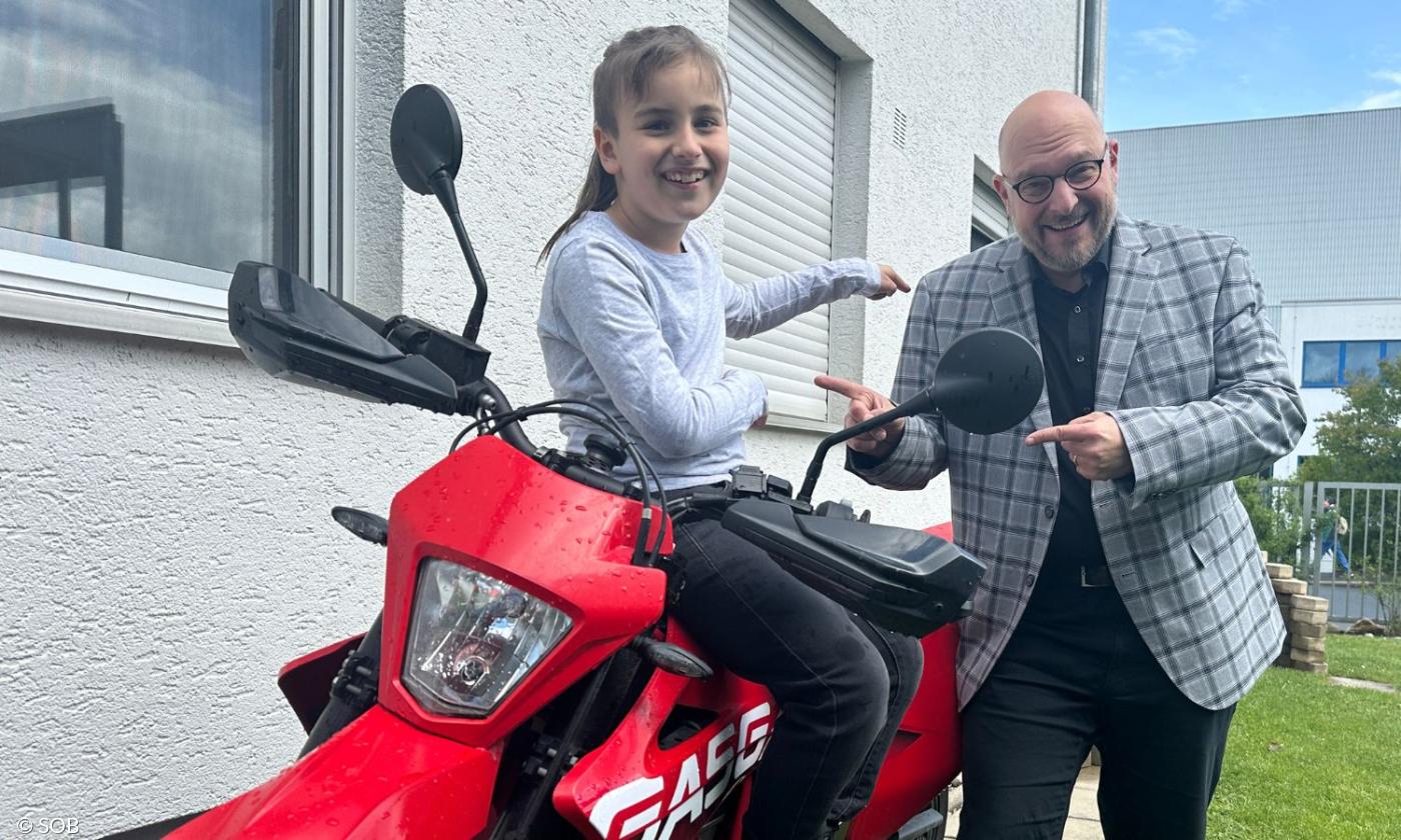 Ein Junge sitzt auf einem Motorrad, ein Mann steht neben ihm