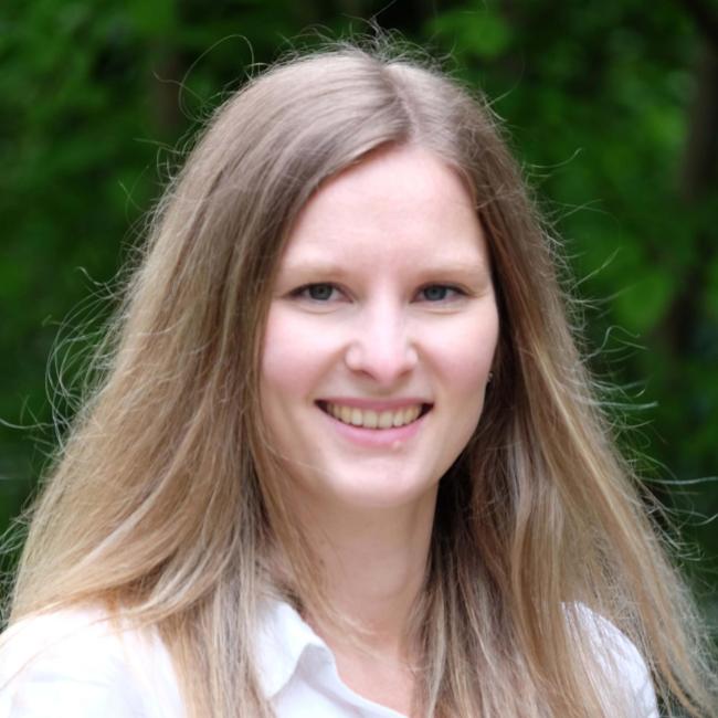 Ein Porträt von Esther Ferstl. Sie ist eine Frau, Ende zwanzig mit dunkelblonden, langen Haaren. Sie lächt in die Kamera. 