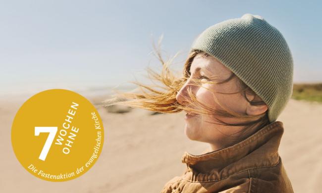 Eine Frau steht mit wehenden Haaren am Strand