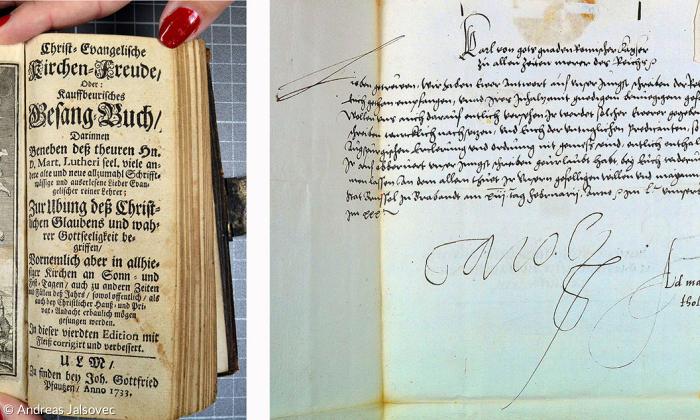 Links ein evangelisches Gesangbuch aus dem 18. Jahrhundert. Daneben ein Brief des katholischen Kaisers Karl V. an die Stadt Kaufbeuren aus dem Jahr 1535.