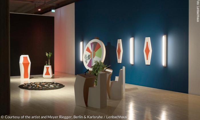 Ausstellungsansicht »After the Fact. Propaganda im 21. Jahrhundert«: John Miller, The Lubgurious Game (Das Finstere Spiel), 1998/2017, Installation, Holz, Acrylfarbe, Wandfarbe, Erde, Plastikpflanze, Dildos, Zeitungen, Euroscheine.