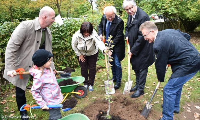 Pflanzaktion in Hirschaid. Gepflanzt wurde er von den Kindern, Kita-Leiterin Karin Krabbes, Fred Schäfer (Diakonie Bamberg-Forchheim, links), tatkräftig unterstützt von (v. l.) Bambergs Dekan Hans-Martin Lechner, dem stellvertretenden Bamberger Landrat Rüdiger Gerst und Hirschaids 3. Bürgermeister Hans Wichert. 