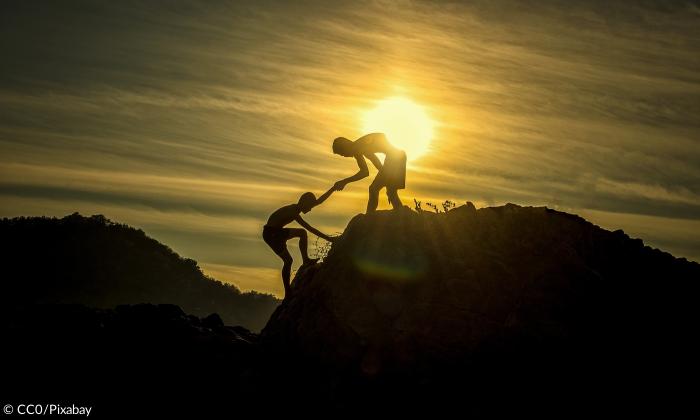 Zwei Jungen helfen sich gegensetig einen Berg zu erklimmen 