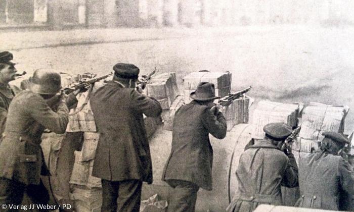 Stahlhelm, Mütze, Hut – Revolutionäre hinter Barrikaden aus Zeitungsstapeln: Im Berliner Zeitungsviertel wurde während des Spartakusaufstands im Januar 1919 besonders heftig gekämpft.
