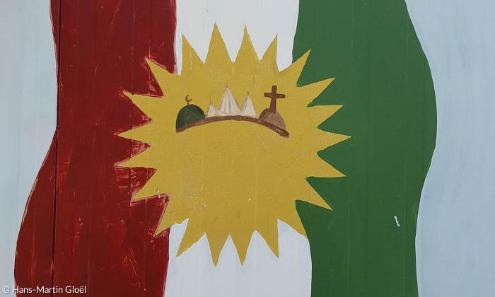 Traum von einer Versöhnung der Religionen: die Kurdische Flagge, in der Sonne die Symbole der Muslime, der Jesiden und der Christen.
