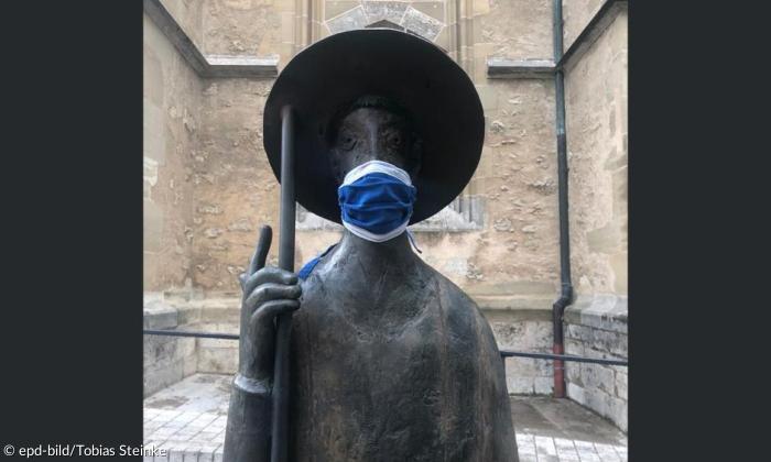 Die Pilgerfigur von Steinacker mit coronabedingtem Mundschutz vor der Rothenburger Jakobskirche