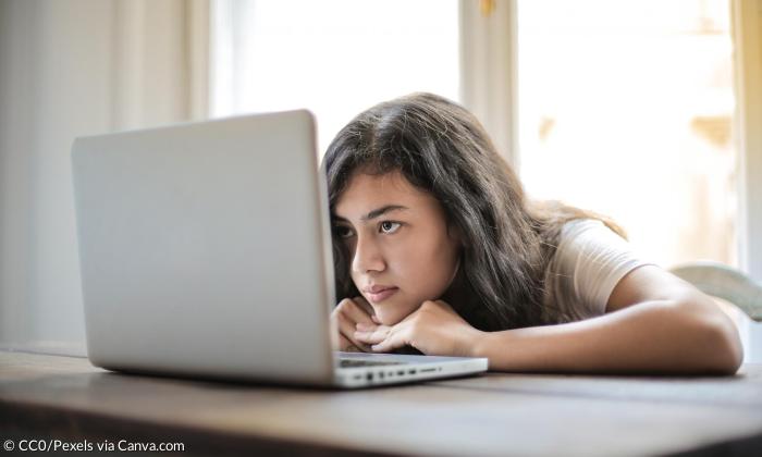 Eine junge Frau schaut auf ihren Laptop-Bildschirm, ihr Gesichtsausdruck ist eher missbilligend