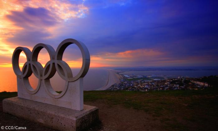 Die olympischen Ringe aus Beton. Sie tronen über einer Stadt. Die Sonne geht gerade auf.