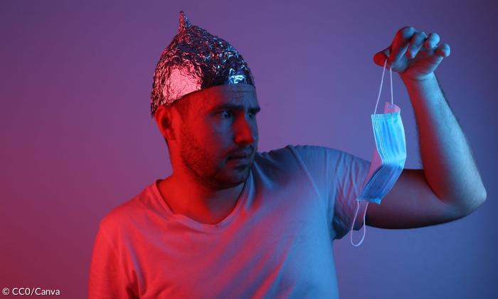 Ein Aluhutträger mit einem Mund-Nasen-Schutz in der Hand