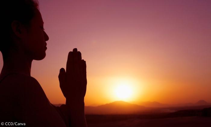 Eine Frau mit gefalteten Händen vor einem Sonnenuntergang