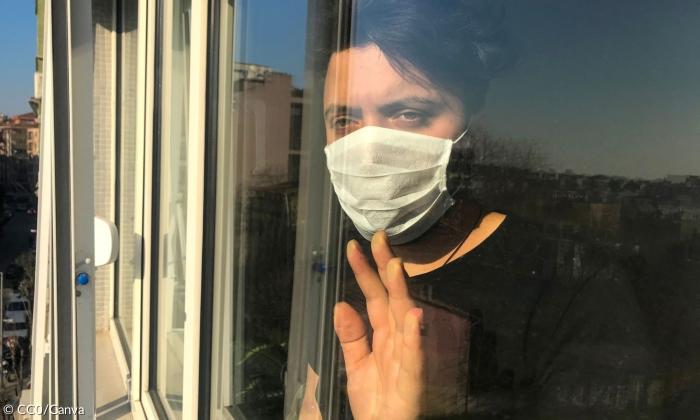 Ein Mann mit Maske hinter einer Glasscheibe