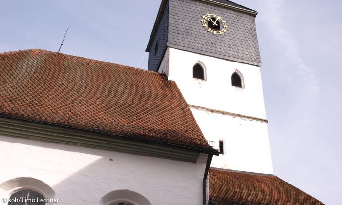 Die Außenfassade der Evangelischen Kirche Weisendorf. Man sieht den Kirchturm und zwei unterschiedlich hohe, schräge Dächer. 
