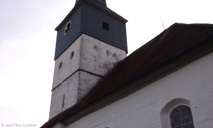 Die Außenfassade der Evangelischen Kirche Weisendorf aus einem anderen Winkel. man sieht den Kirchturm und ein schräges Dach.