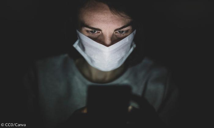 Eine Frau mit einer Maske, die auf einen Handybildschirm blickt.
