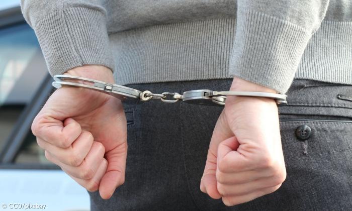 Hände einer Person hinter ihrem Rücken in Handschellen.