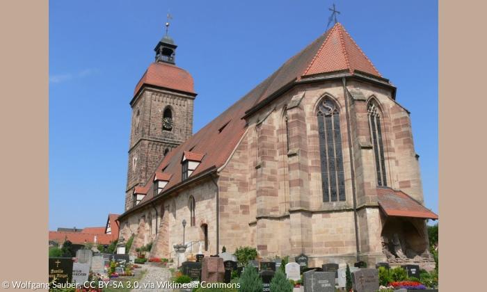 Die evangelische Kirche St. Laurentius in Roßtal. Die Kirche ist aus braunen Steinen gebaut und hat einen Kirchturm mit einer welsche Haube.
