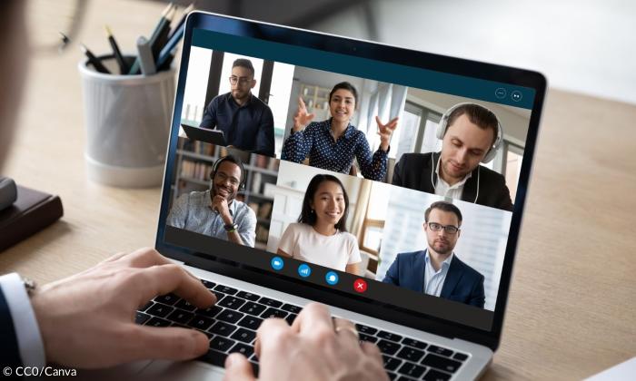 Ein Mensch im Anzug sitzt vor einem Computer, auf dessen Bildschirm mehrere Menschen in einer Videokonferenz zu sehen sind