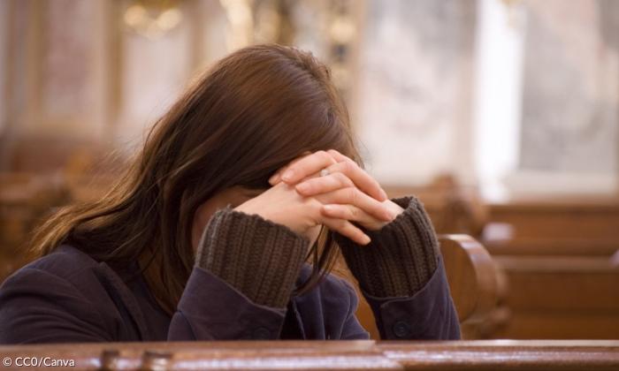 Eine Frau betet in einer Kirche, die Hände vor dem Gesicht gefaltet