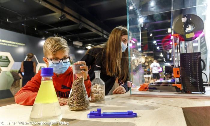Zwei Kinder stehen vor ein paar Flaschen, in denen verschiedene Materialen sind.