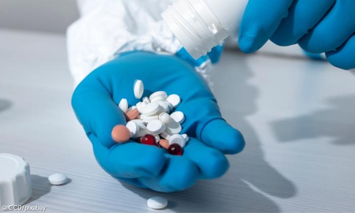 Eine behandschuhte Hand, die Tabletten hhält.