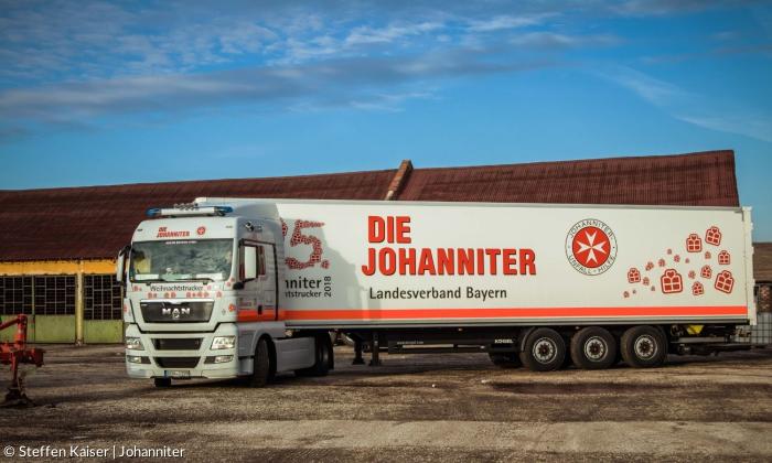 Ein großer Truck, der auf einem Hof steht. An der Seite steht "Die Johanniter", außerdem sieht man das Logo und Geschenke aufgedruckt