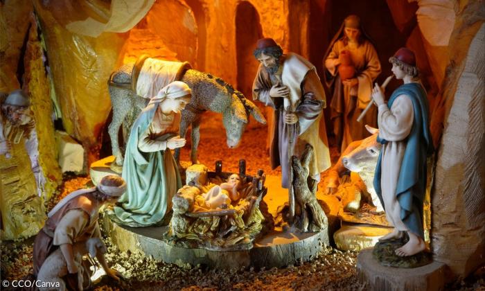 Eine WeIhnachtskrippe mit Jesus, Maria und Joseph. Außerdem ist ein Hirte mit einer Flöte am Start, eine Kuh und ein Esel. Im Hintergrund steht eine Person, die einen Krug in der Hand hält.