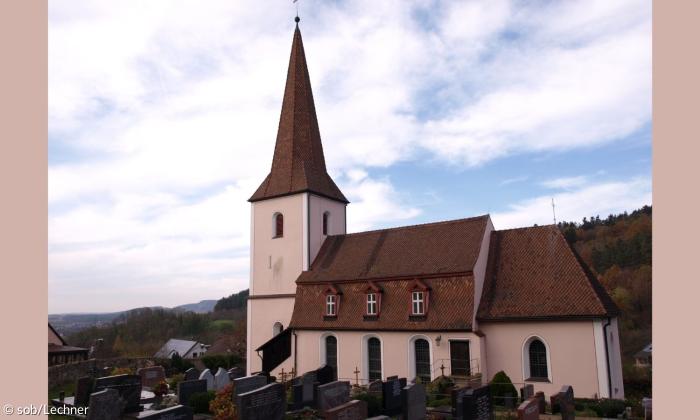 Das lachsfarbene Gebäude der Jakobuskirche in Rüsselberg. Davor ist der Friedhof der Kirche.