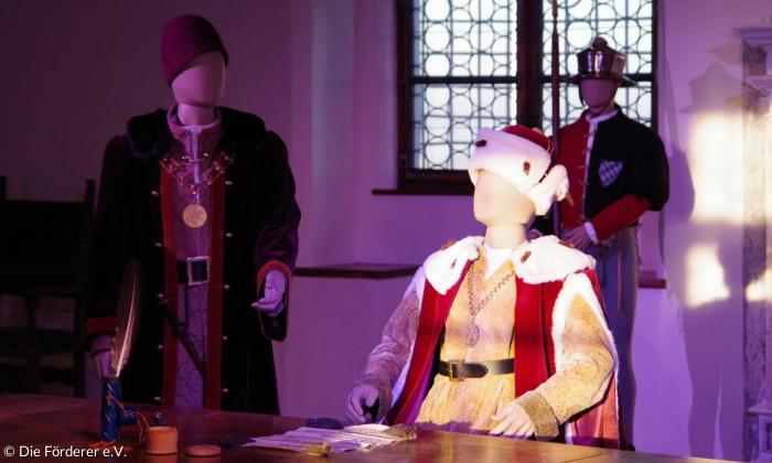 Ein Saal einer Burg. Es sind drei Puppen in historischen Gewändern zu sehen