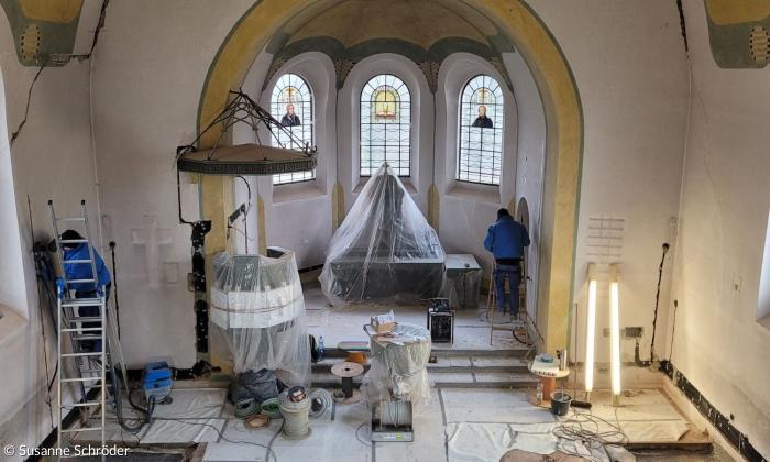 Innenraum der Kirche. Der altar und die Kanzel sind Plastik eingewickelt. Ein Mann auf einer Leiter streicht die Wand.