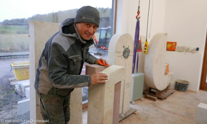 Ein Mann arbeitet an einem Grabstein und schaut den Betrachter an.