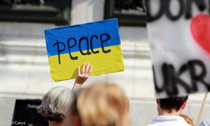 Ein Schild bei einer Demonstration zeigt das Wort "Peace" auf den Farben der ukrainischen Flagge