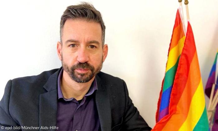 Tobias Oliveira Weismantel neben mehreren Regenbogen-Fahnen