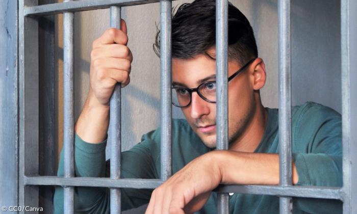 Ein Mann mit Brille hinter Gitterstäben
