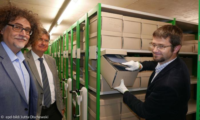 Auf dem Bild stehen drei Männer neben einem Archiv-Regal.