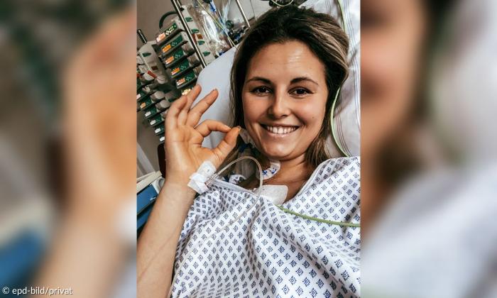 Eine junge Frau liegt in einem Krankenhausbett und lächelt