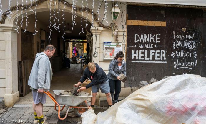 Helfende räumen Schutt weg, im Hintergrund steht "Danke an alle Helfer"