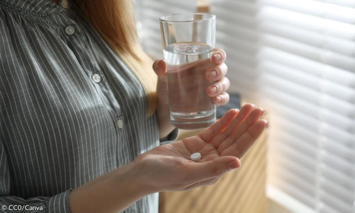 Eine Frau mit einer Pille und einem Glas Wasser in den Händen