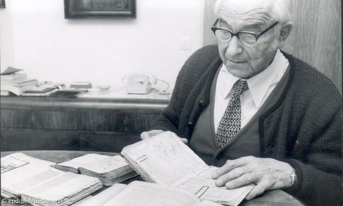 Pfarrer Karl Steinbauer mit mehreren Büchern an einem Tisch