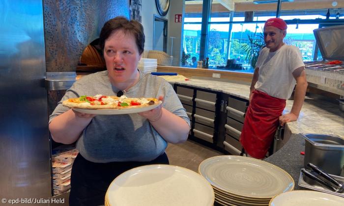 Eine junge Frau mit einer Pizza, dahinter ein Mann