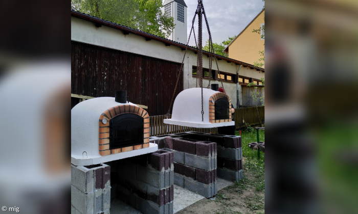 Zwei Pizzaöfen stehen auf einigen zusammen gemauerten Steinen. Im Hintergrund sieht man einen längeren Schuppen, der ihn fast vollkommen bedeckt.
