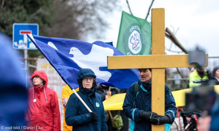 Zwei Menschen in Regenjacke mit Friedensflagge und gelbem Kreuz.