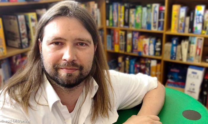 Ein Mann mit langen Haaren und Bart vor einer Bücherwand