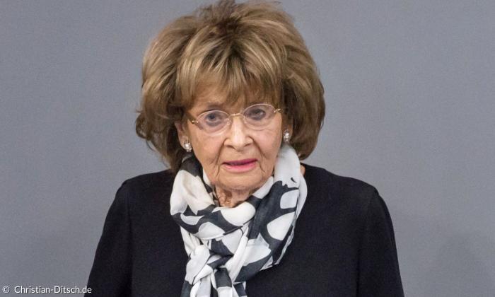 Porträt einer älteren Dame mit braunem vollen Haar und Brille trägt einen schwarzen Blazer und einen schwarz-weiß gemusterten Schal