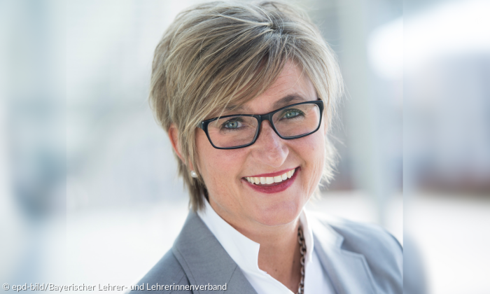 Porträt-Aufnahme einer Frau Mitte Anfang 50, die frontal in die Kamera blickt. Sie trägt eine Brille sowie kürzere dunkel-blonde Haare.