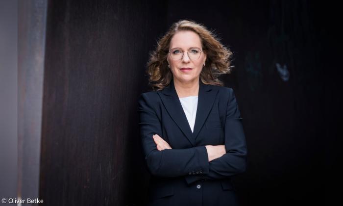 Eine Frau im dunklen Blazer, die Arme verschränkt