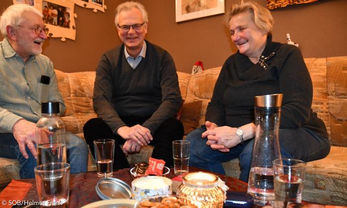 Drei Menschen sitzen an einem Wohnzimmertisch