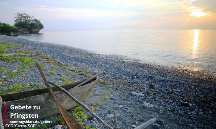 Ein Boot liegt auf einem Kiesstrand, dahinter geht die Sonne unter