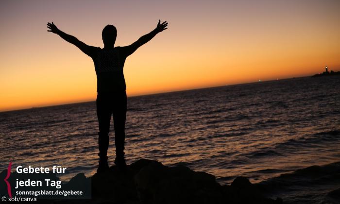 Ein Mensch steht am Meer und hebt die Arme